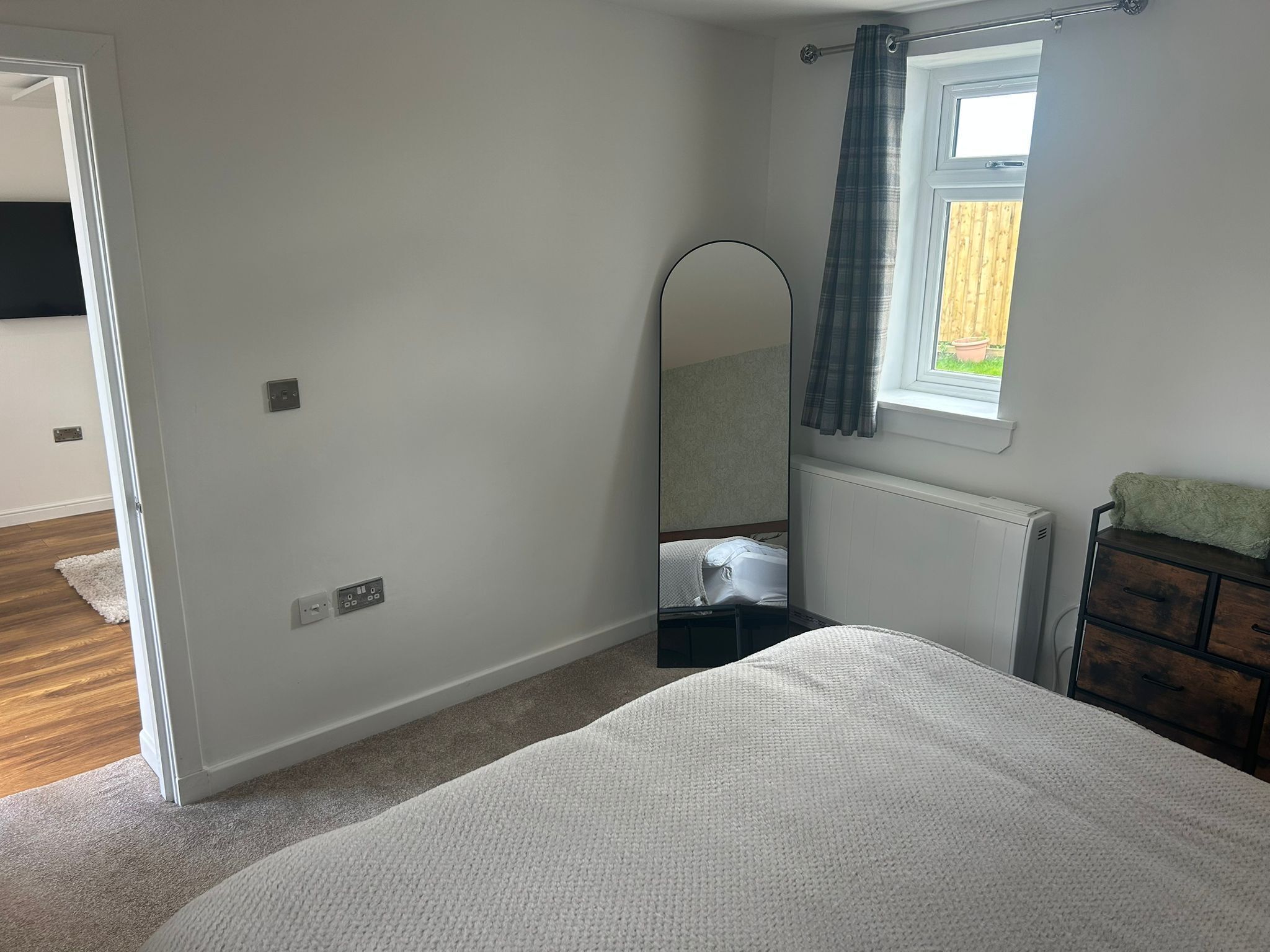 A bedroom with a bed, a dresser, a mirror, and a window with curtains.