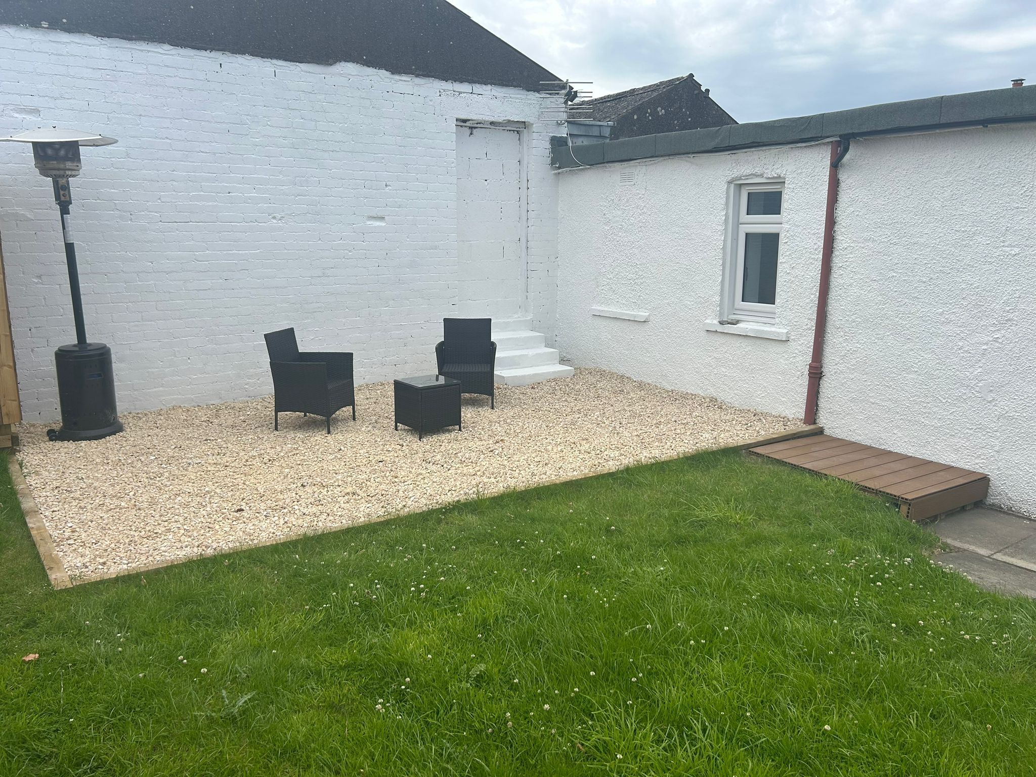 A white house with a gravel patio, two black chairs, and a small wooden deck.