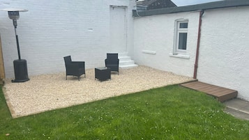 A white house with a gravel patio, two black chairs, and a small wooden deck.