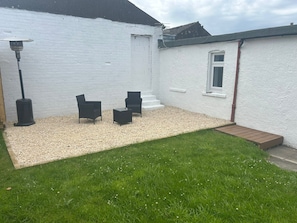 A white house with a gravel patio, two black chairs, and a small wooden deck.
