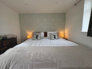 Un lit bien fait, avec une couvre-lit à motifs, deux lampes de chevet et une tête de lit ornée d’un panneau décoratif.