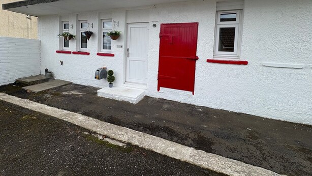 A white building with a red door, windows with hanging flower baskets, and a small step leading to the entrance. - Muirside Cottage - sleeps 3 guests  in 1 bedroom (Stirling)