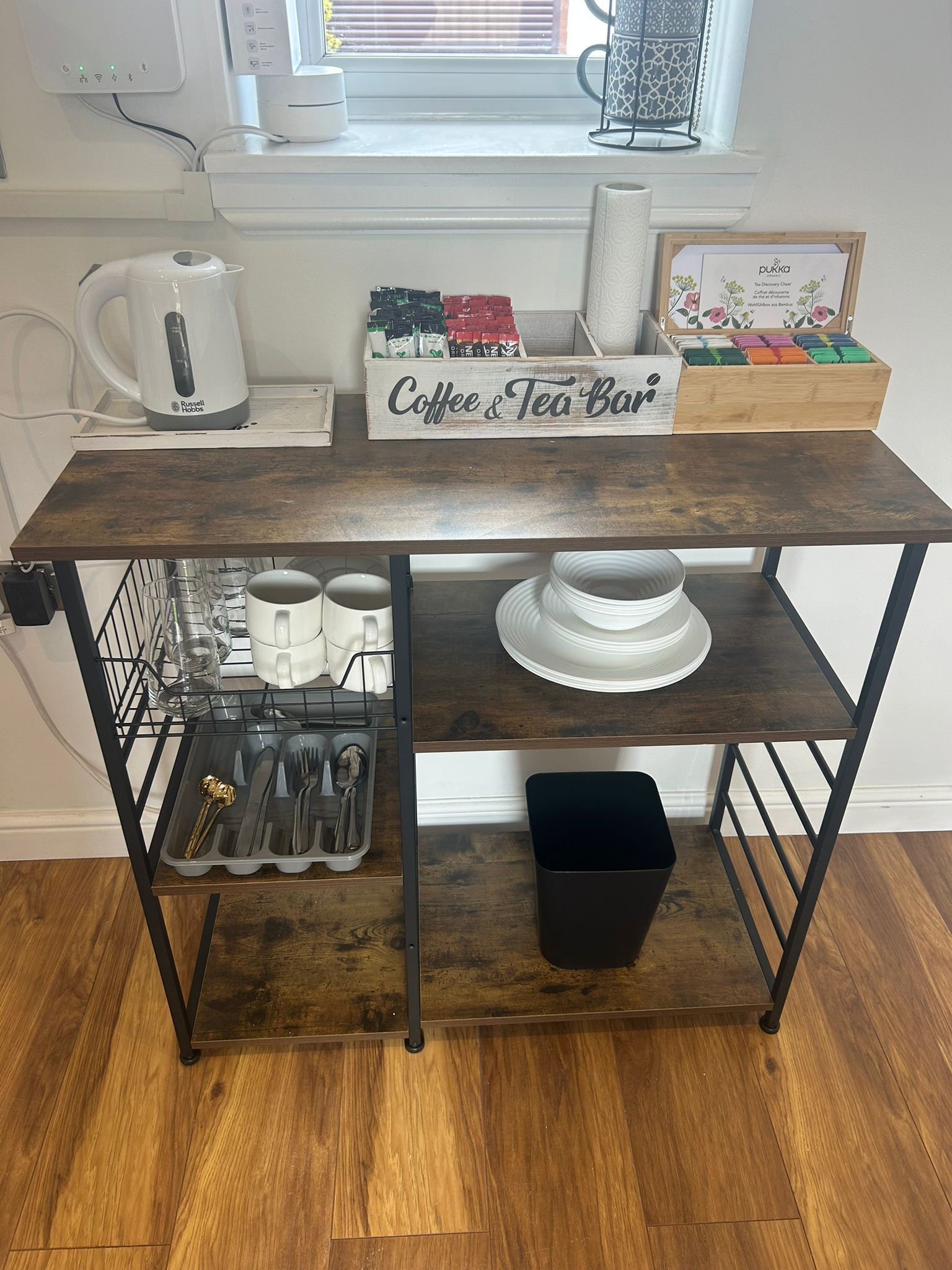 A wooden coffee and tea bar with storage shelves, a kettle, and a tea infuser.