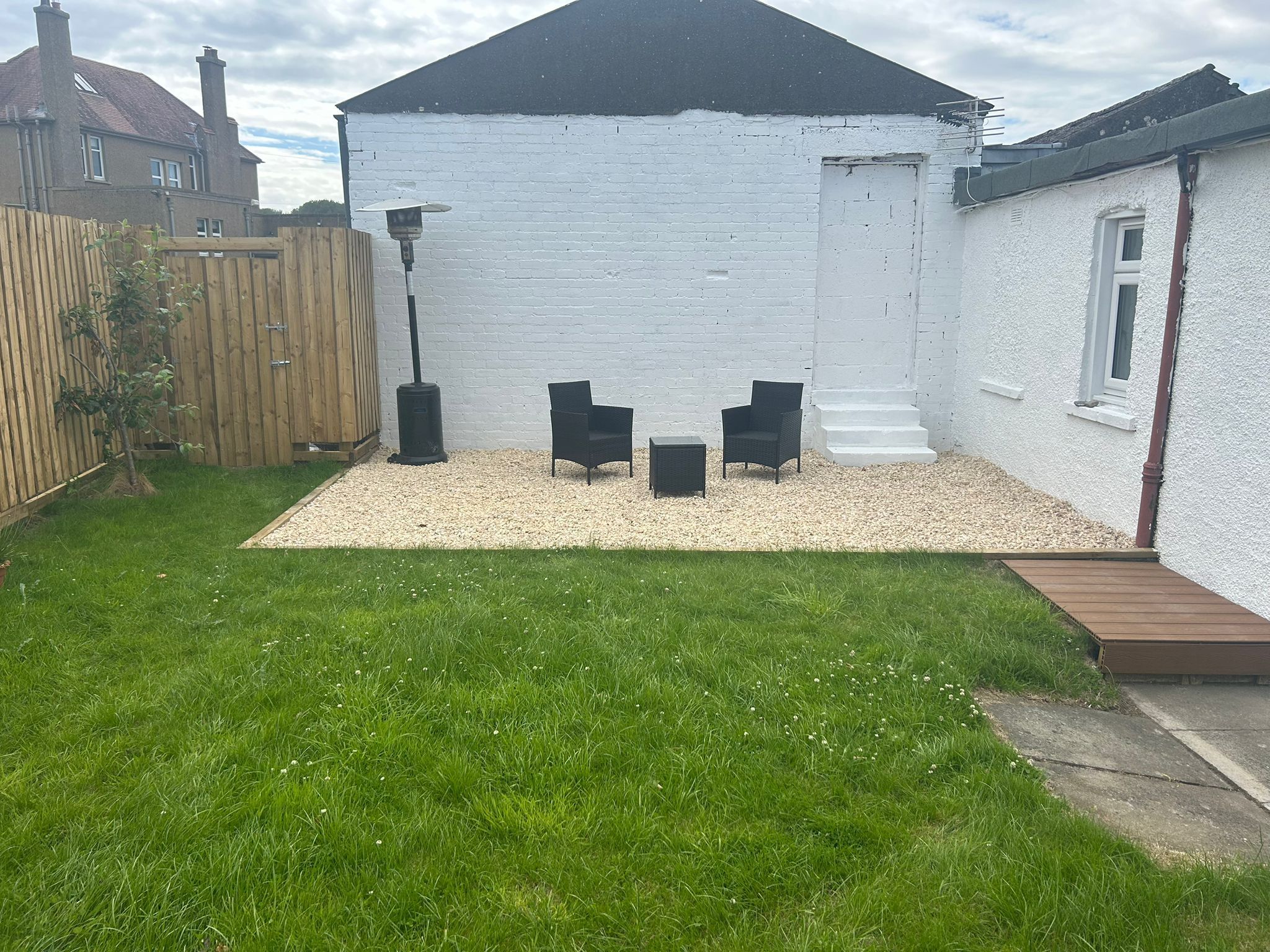 A white building with a black roof, a gravel patio, and a wooden fence.
