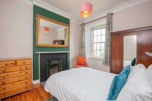 A bedroom with a bed, dresser, mirror, fireplace, and window. - Banrigh House - a terrace that sleeps 6 guests in 3 bedrooms (Stirling)