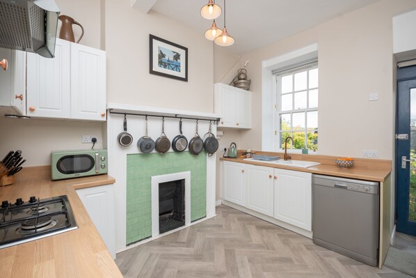 A modern kitchen with white cabinets, a green tiled fireplace, hanging pots, and a dishwasher. - Banrigh House - a terrace that sleeps 6 guests in 3 bedrooms (Stirling)