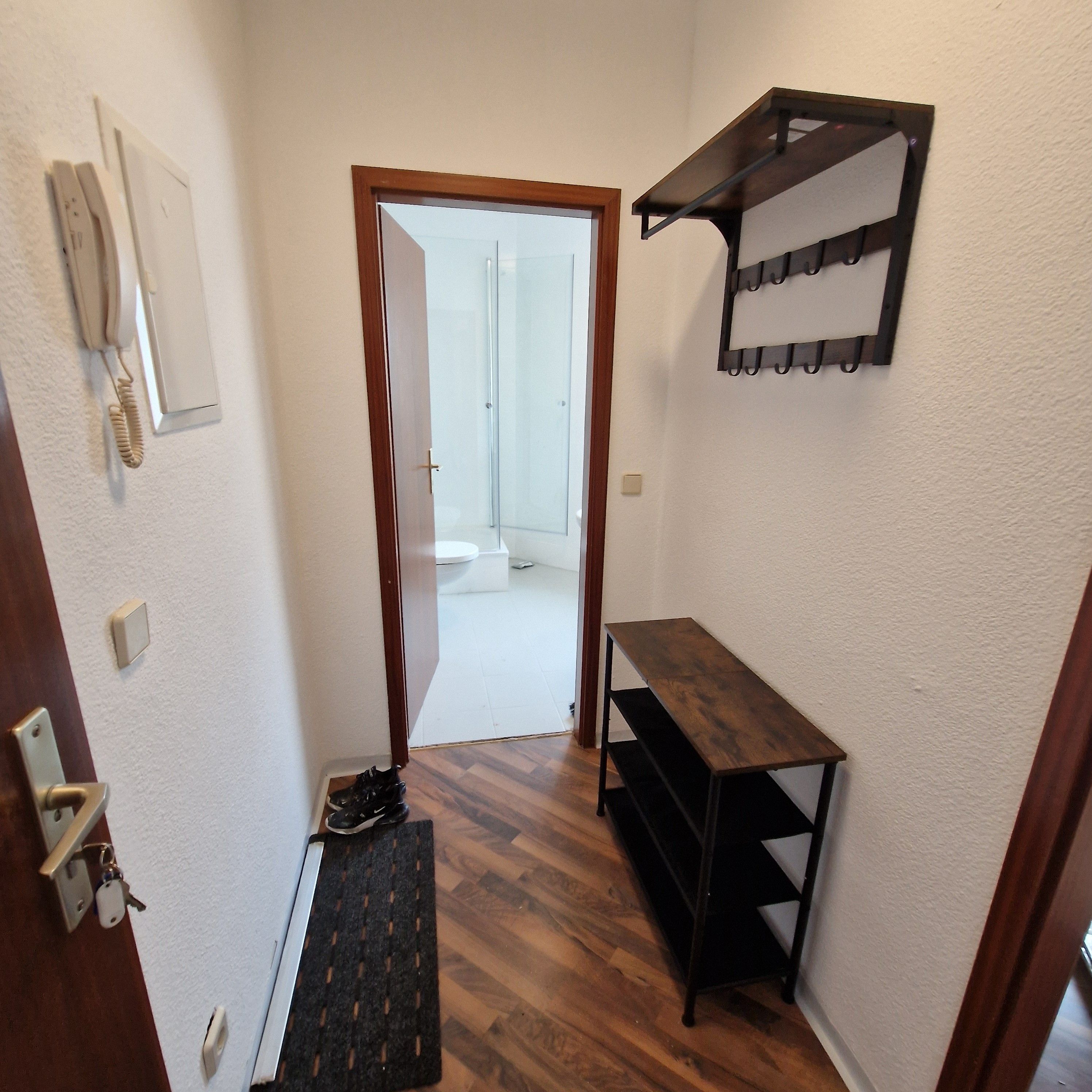 Ein Flur mit einer Holztür, einem Kleiderständer, einem Telefon und einem kleinen Tisch.