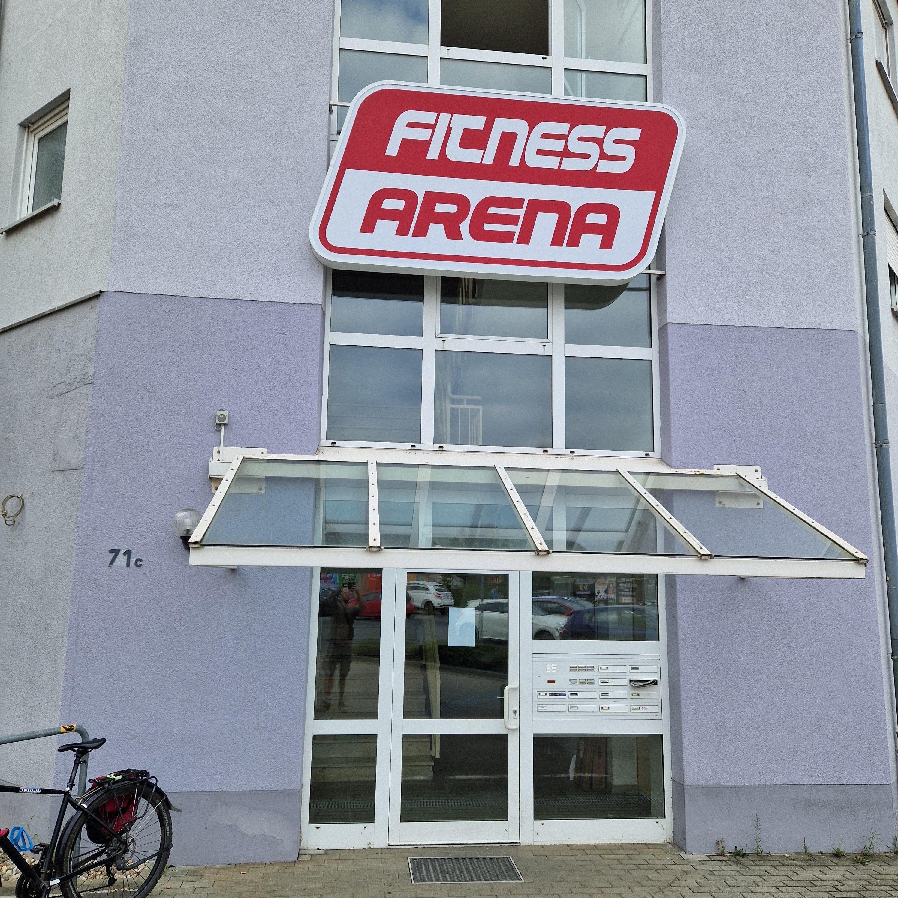 En byggnad med en skylt ovanför ingången där det står ”Fitness Arena”.