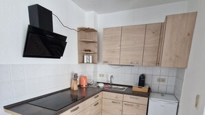 A compact kitchen with a black microwave, wooden cabinets, a sink, and a white dishwasher. - Apartment "Sala Uno" with Wi-Fi (Coswig)