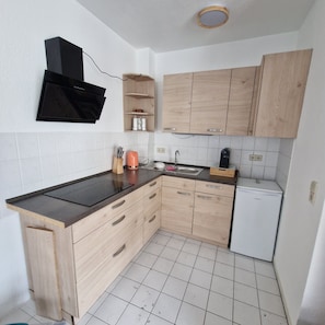 A compact kitchen with a black microwave, wooden cabinets, a sink, and a white dishwasher. - Apartment "Sala Uno" with Wi-Fi (Coswig)