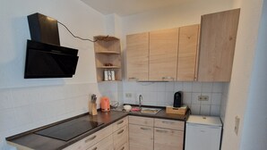 A compact kitchen with a black range hood, wooden cabinets, a small white refrigerator, and a tiled floor.