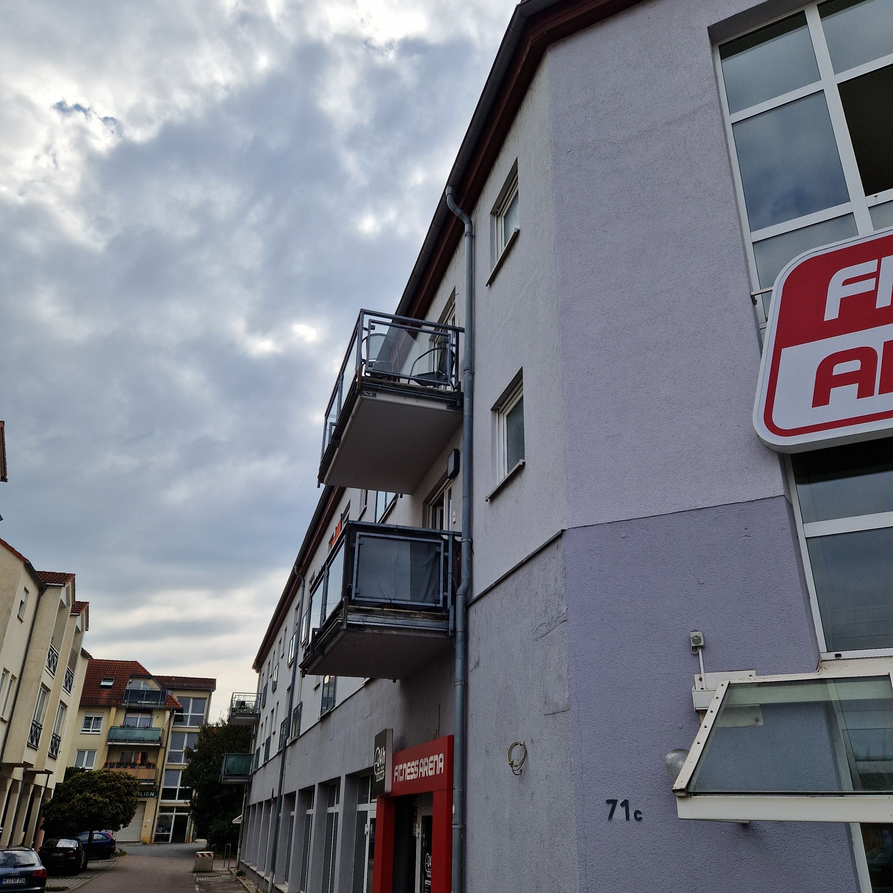 Ein mehrgeschossiges Gebäude mit Balkonen, einem sichtbaren Schaufenster und blauem Himmel.
