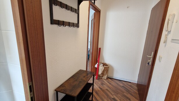 A hallway with a wooden bench, a coat rack, and a door with a phone.