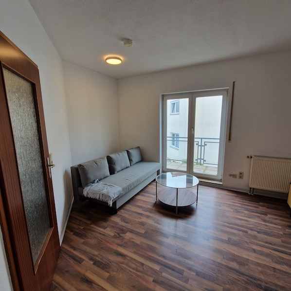 A room with a sofa, a glass coffee table, wooden flooring, a door, and a window with a view. - Apartment "Sala Uno" with Wi-Fi (Coswig)