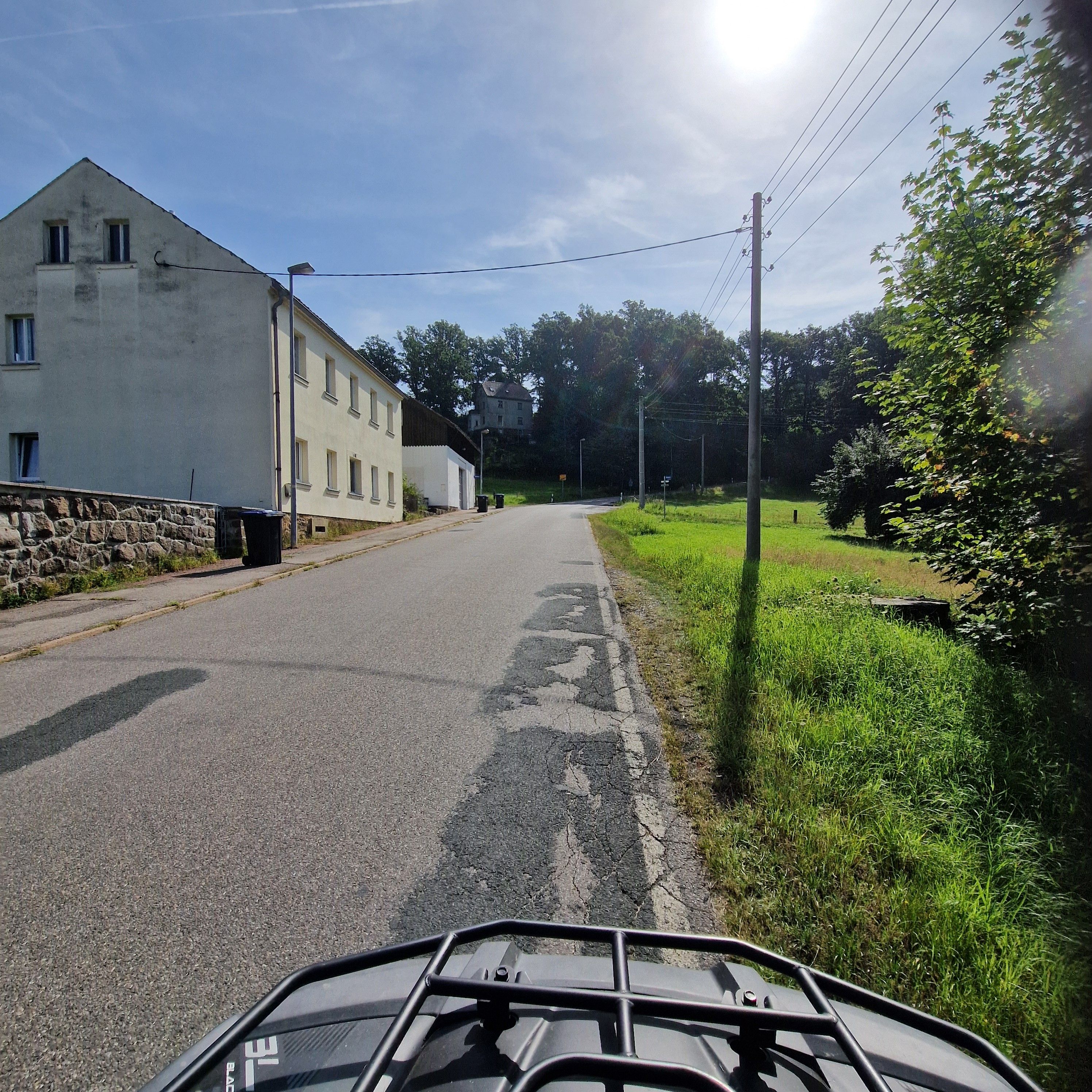 Eine Landstraße mit einem weißen Gebäude links und einem grünen Feld rechts.