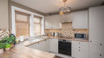 A modern kitchen with white cabinets, a wooden countertop, a built-in oven, and a microwave.