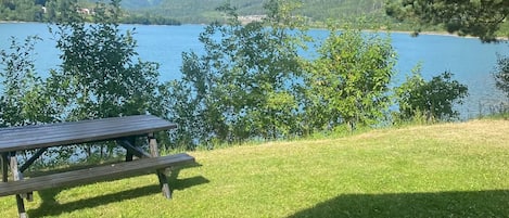 A picnic table on a grassy area with a view of a lake and hills in the background.