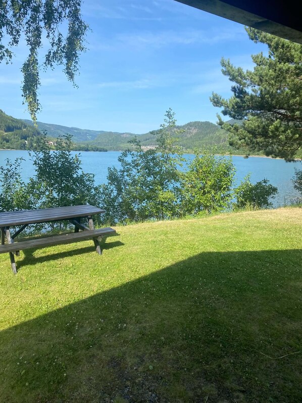 A picnic table on a grassy area with a view of a lake and hills in the background.