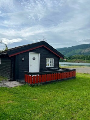 A cabin with a red porch and a white door, surrounded by a grassy area and a river.