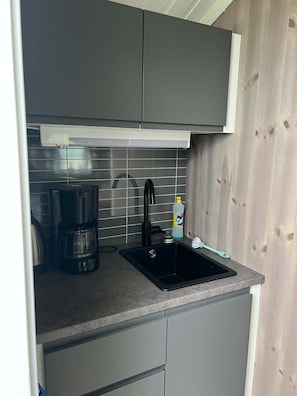 A compact kitchen with a single sink, a coffee maker, and a bottle of hand soap.