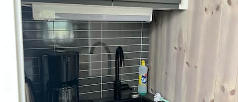 Una cocina compacta con un lavamanos, una cafetera y una botella de jabón para manos.