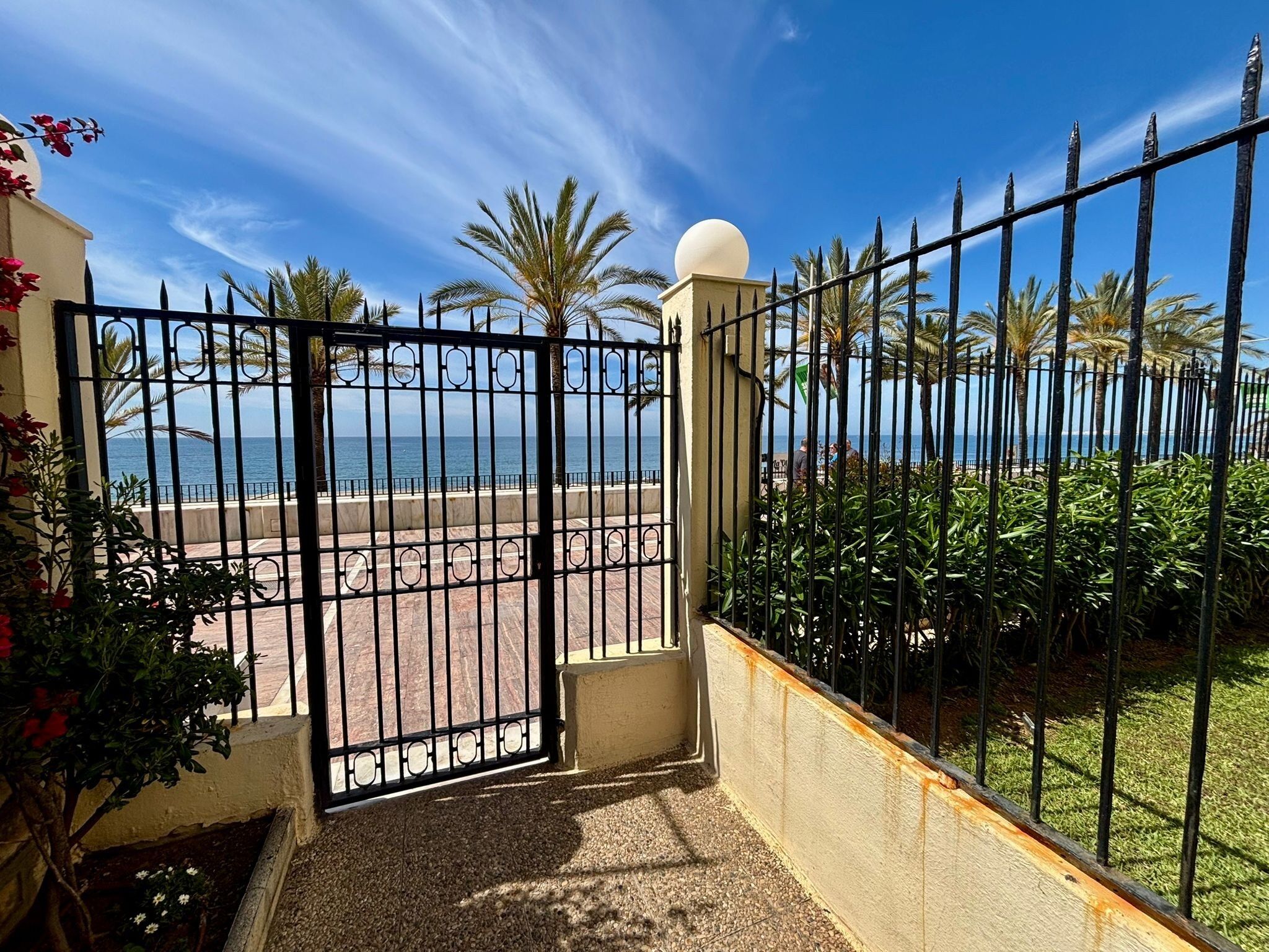 A gated entrance to a property with a view of the beach and palm trees.