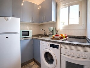 A compact kitchen with a washing machine, a microwave, and a coffee maker. - Apolo Mediterranean Living (Marbella)