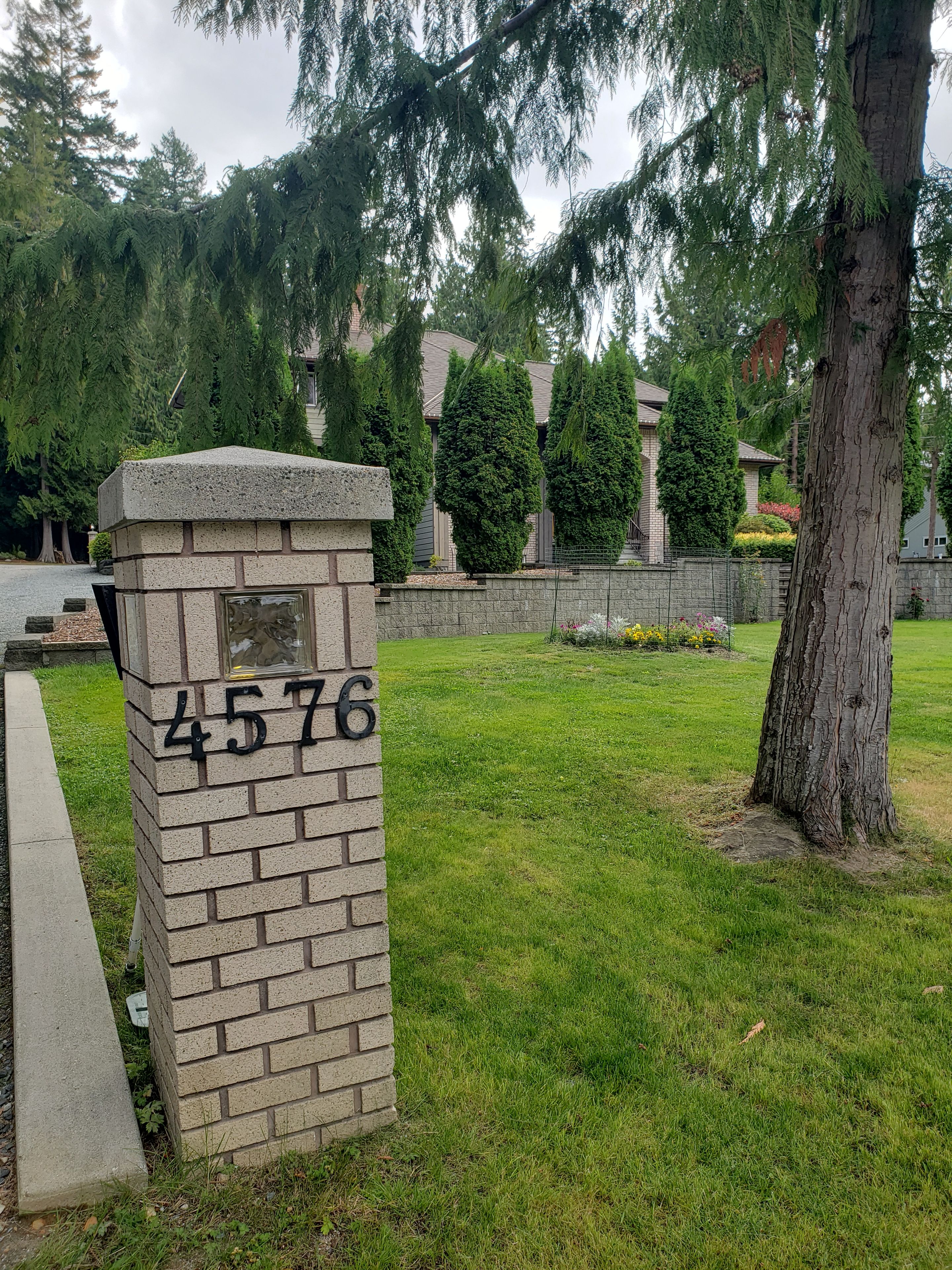 Une boîte aux lettres en pierre portant le numéro 4576, entourée d’herbe et d’arbres.