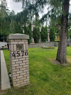 A stone mailbox with the number 4576, surrounded by grass and trees. - Quiet, private brand new 1 bdm on Wooded Estate by shops, airport & beach (Powell River)
