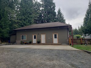 A single-story building with a sloped roof, a front porch, and a gravel driveway. - Quiet, private brand new 1 bdm on Wooded Estate by shops, airport & beach (Powell River)