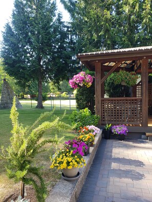 A wooden pergola with hanging flower baskets, a paved walkway, and a variety of potted plants. - Quiet, private brand new 1 bdm on Wooded Estate by shops, airport & beach (Powell River)