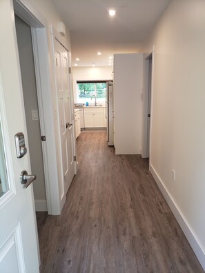 A hallway with wooden flooring leading to a kitchen area with white cabinets and a window. - Quiet, private brand new 1 bdm on Wooded Estate by shops, airport & beach (Powell River)
