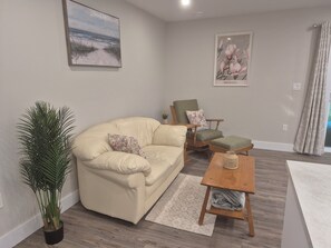 A living room with a beige sofa, a wooden rocking chair, a small table, and a potted plant.