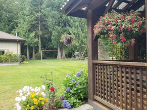 A wooden deck with a lattice railing, a grassy yard, and a swing set. - Quiet, private brand new 1 bdm on Wooded Estate by shops, airport & beach (Powell River)