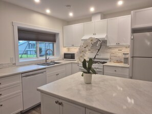 A modern kitchen with white cabinetry, a stainless steel refrigerator, a built-in microwave, and a gas stove.