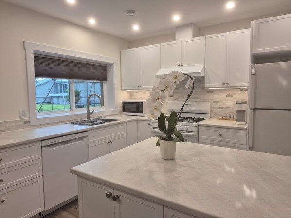 A modern kitchen with white cabinetry, a stainless steel refrigerator, a built-in microwave, and a gas stove. - Quiet, private brand new 1 bdm on Wooded Estate by shops, airport & beach (Powell River)