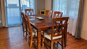 Un coin repas avec une table et des chaises en bois, un luminaire au plafond et de grandes fenêtres avec des rideaux.