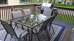 Une terrasse dotée d’une table et de chaises à plateau en verre, d’un barbecue et d’un tapis à motifs.
