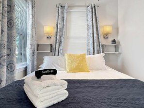 A neatly made bed with a black and white quilt, a yellow pillow with 'Drift Away' text, and a stack of white towels. - Cozy Vermilion Retreat Near Lake Erie - Sleeps 3 (Vermilion)