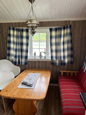 Une pièce chaleureuse avec une table en bois, une chaise blanche, un canapé rouge et des rideaux à carreaux.