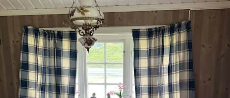 A cozy room with a wooden table, a white chair, a red sofa, and plaid curtains.