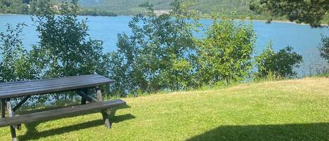 A picnic table on a grassy area with a view of a lake and hills in the background.