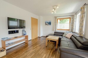 A living room with a flat-screen TV, wooden furniture, a sofa, and a window with curtains. - Rauris House, Hohe Tauern National Park (Rauris)