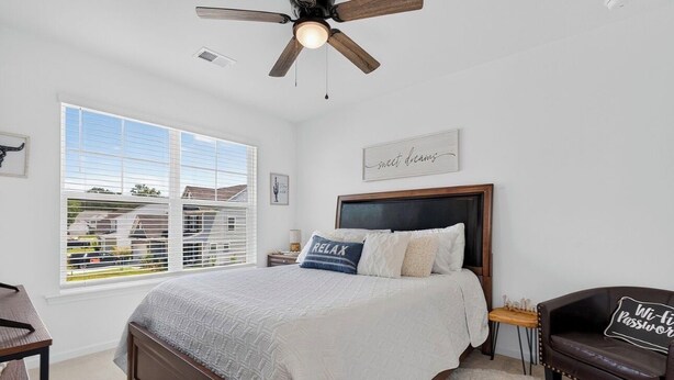 Quarto com uma cama grande, ventilador de teto, janela com persianas e vista para um bairro.