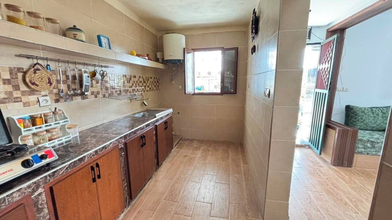 Une cuisine avec un mur recouvert de carreaux, des armoires en bois, un plan de travail avec une cuisinière et une fenêtre donnant sur un beau paysage.