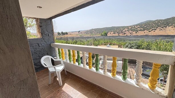 Ein Balkon mit weißer Brüstung, einem weißen Stuhl und Blick auf einen Weinberg.