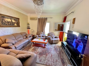 Una sala de estar con sofá, sillones, mesa de centro, televisor y candelabro.