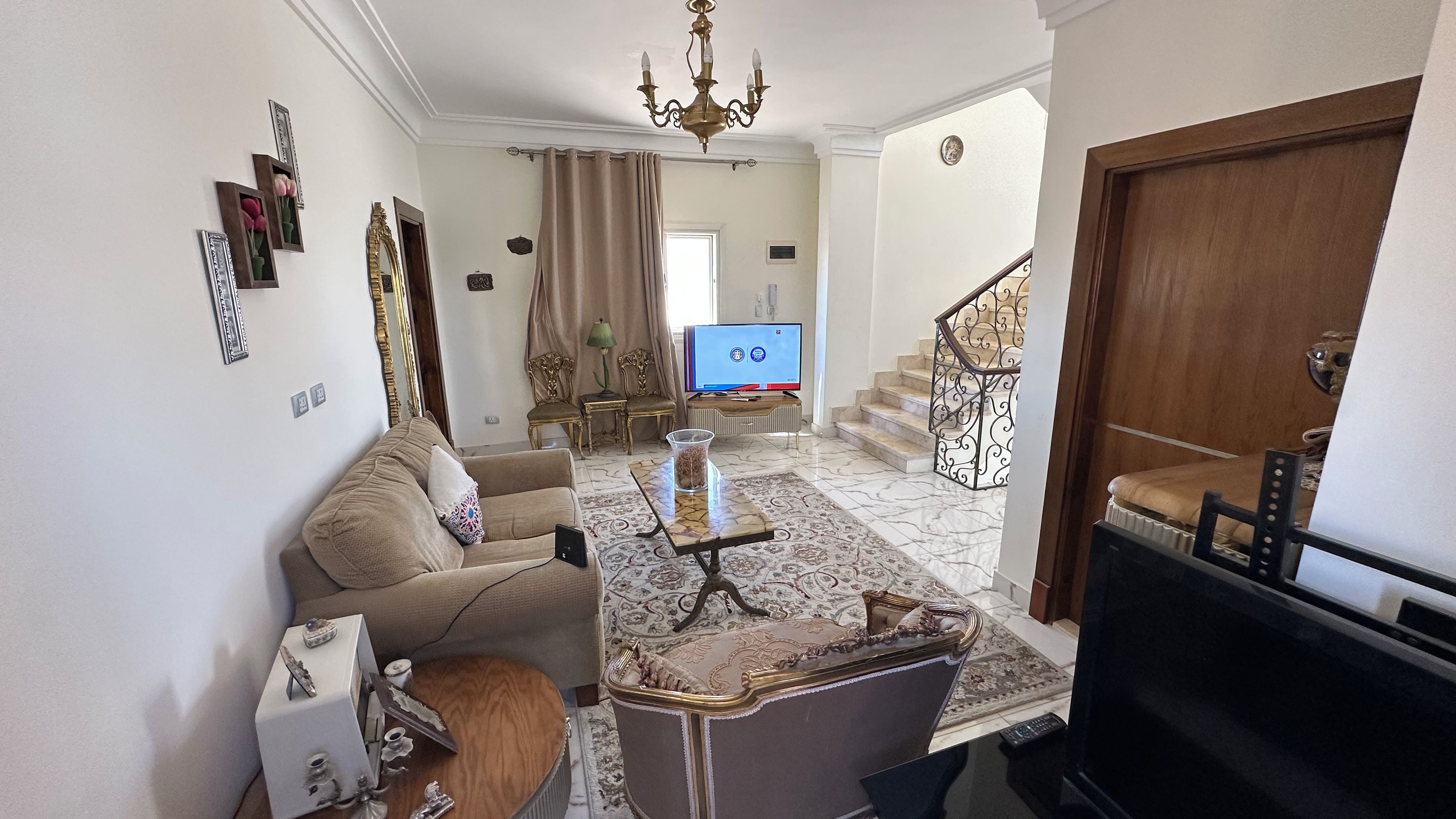 A living room with a sofa, a coffee table, a TV, and a staircase.
