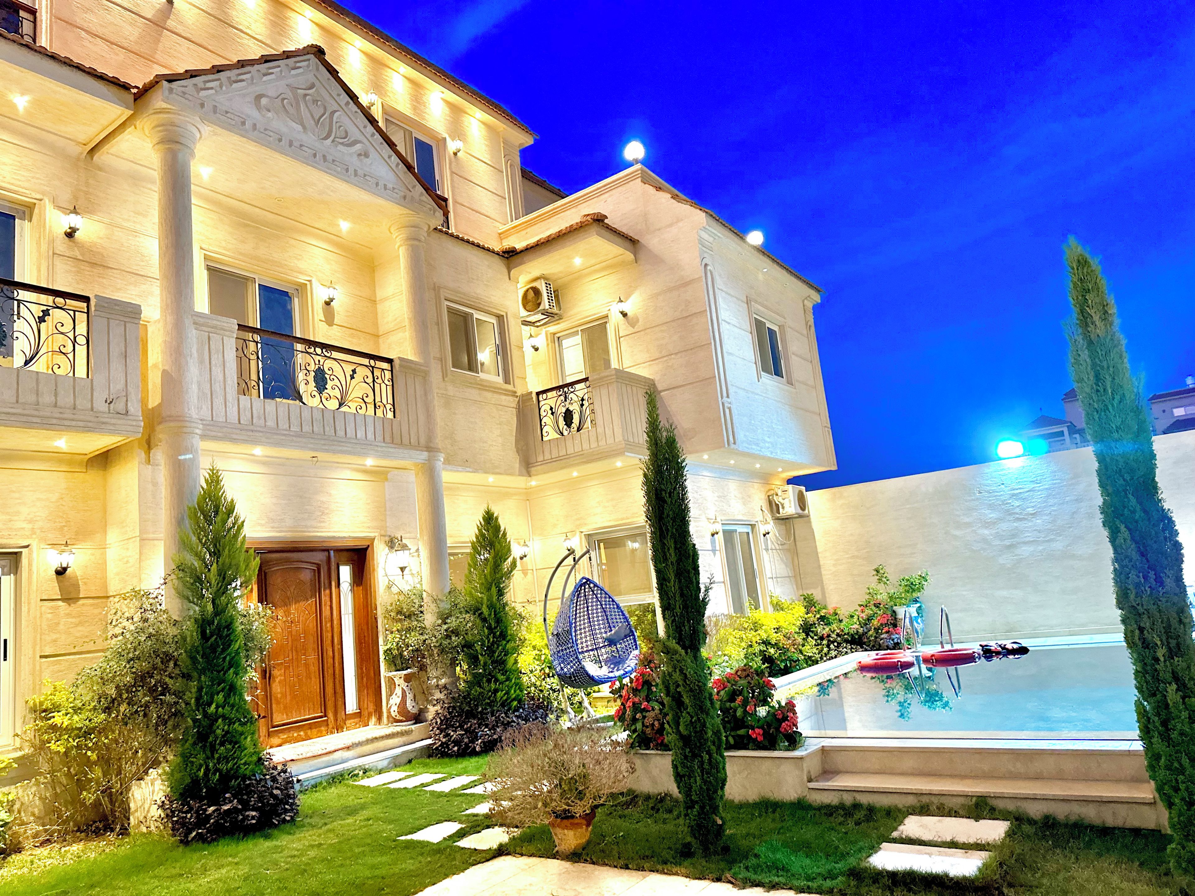 A multi-story hotel with a swimming pool, outdoor lighting, and a well-maintained garden.