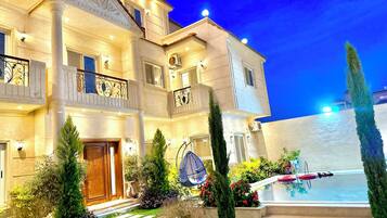 A multi-story hotel with a swimming pool, outdoor lighting, and a well-maintained garden.